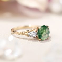 a close up of a ring with a green stone and two white diamonds on it