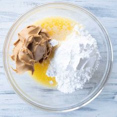 two ingredients in a glass bowl on top of a white wooden table, one is yellow and the other is brown