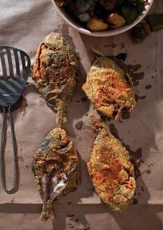 four pieces of fried chicken sitting on top of a table next to a bowl of vegetables