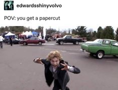 a young man is dancing in the middle of a parking lot with other cars behind him