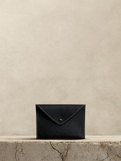 a black leather wallet sitting on top of a stone slab with a white wall in the background