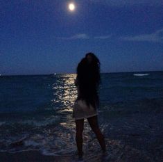 a woman standing in the ocean at night with her hair blowing back to the side