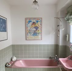 a pink bath tub sitting next to a sink in a bathroom under a painting on the wall