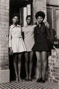 three women standing next to each other in front of a brick building