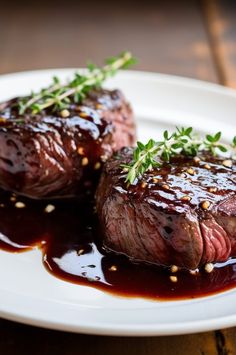 two steaks on a plate with sauce and garnish