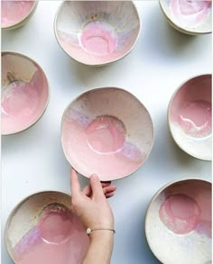 pink and white bowls are being held by a woman's hand in front of them