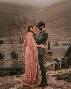 a man and woman standing next to each other on top of a rock covered hillside