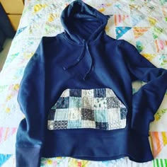 a blue hoodie with patchwork design on the front and side, sitting on a quilted bedspread