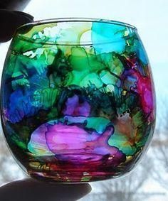 a hand holding a colorful glass in front of a window