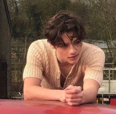 a young man leaning on the hood of a red car with his hands folded out