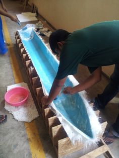 a man in green shirt working on a surfboard with blue and white foam around it