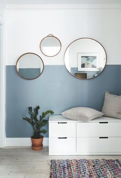 three round mirrors hanging on the wall above a white dresser in a blue and white room