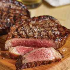 two pieces of steak sitting on top of a wooden cutting board