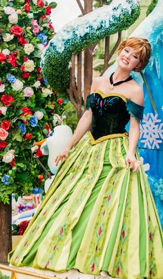 a woman in a green and yellow dress standing next to a snowman statue at disneyland world