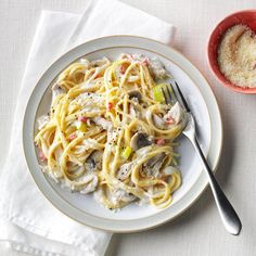 a white plate topped with pasta next to a bowl of grated parmesan cheese