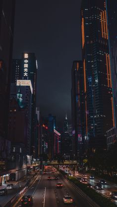 a city street at night with lots of tall buildings and cars driving down it's sides