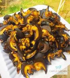 a white plate topped with mussels on top of a wooden table next to grass