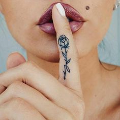 a woman holding her finger up to her nose with a rose tattoo on it's thumb