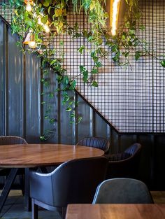 a restaurant with wooden tables and chairs next to a metal wall covered in green plants