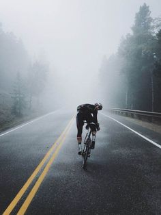 a bicyclist is riding down the road on a foggy day