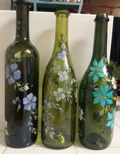 three green bottles with flowers painted on them sitting on a counter top next to each other