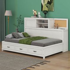 a white bed with drawers underneath it in a green room next to a rug on the floor