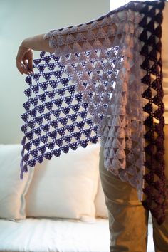 a woman holding up a crocheted shawl in front of a couch with pillows