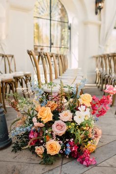 an arrangement of colorful flowers on the ground in front of chairs and tables at a wedding