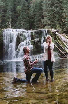 a man kneeling down next to a woman in front of a waterfall while she holds her head