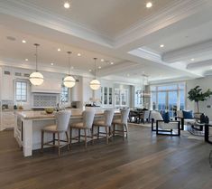 a large open kitchen and dining room with white walls, wood floors and ceiling lights