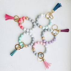 several different colored beads and tassels on a white surface with gold rings around them