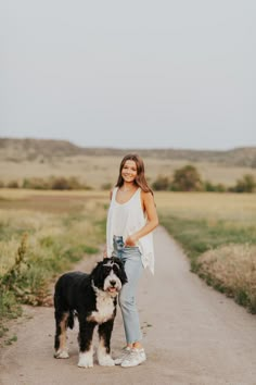 a woman standing next to a black and white dog on a dirt road in the middle of nowhere