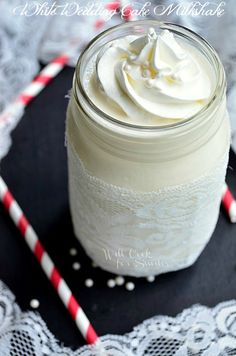 a glass jar filled with whipped cream on top of a doily next to two red and white striped straws