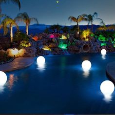 an outdoor pool with lights around it and palm trees in the background at night time