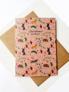 a pink christmas card with cats and trees on it, sitting on top of a brown envelope