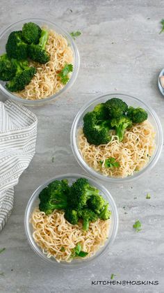 three bowls filled with noodles and broccoli on top of a white tablecloth