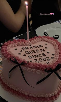 a pink heart shaped birthday cake with a lit candle