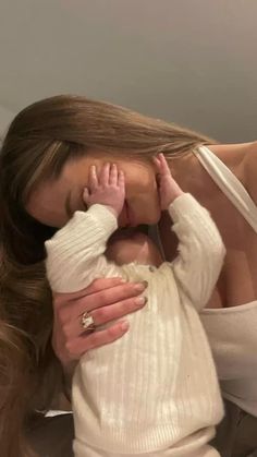 a woman holding a baby in her arms and kissing it's face with both hands