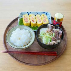 a wooden plate topped with rice, meat and veggies next to chopsticks