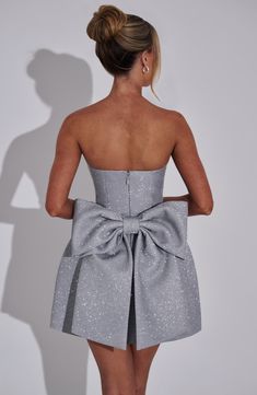 THE dress of the season has landed and you're going to be obsessed. Meet Alice, our dreamy sparkly mini with a pretty bubble shaped skirt and waist cinching bodice. This strapless style is complete with an oversized bow to the back for perfect feminine drama. 



Colour: Silver Sparkle.

Premium non-stretch glitter woven fabric.

Fully lined.

Strapless neckline.

Waist cinching.

Detachable, oversized bow detail to back.

Voluminous bubble shaped skirt.

Lace up to the reverse.

Invisible zipper.

Mini length.

Model is an XS and is wearing an XS.

 Size: XS, S, M, L, XL, XXL Short Bubble Dress, Short Winter Formal Dresses, Short Dress With Bow, Winter Formal Dresses Short, 18th Birthday Dress, Freshman Hoco Dresses, Formal Dress Short, Dance Fits, Bow Dresses