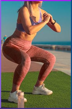 a woman is doing squats on the grass by the beach with her hands behind her back