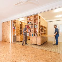 two men are standing in an empty room with bookshelves on the walls and wooden floors