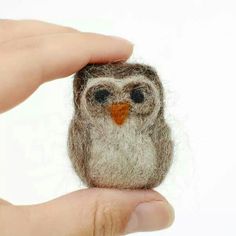 a small stuffed owl sitting on top of someone's hand in front of a white background