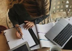 a woman sitting at a table writing on a piece of paper with a laptop next to her