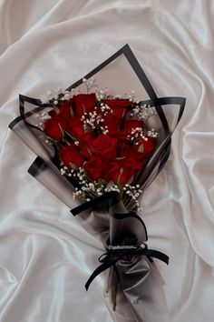 a bouquet of red roses wrapped in black ribbon on a white satin sheet with an ornament