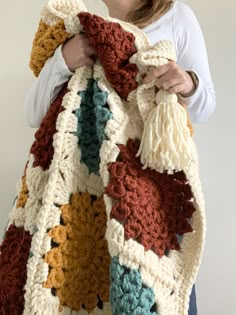 a woman is holding up a crocheted blanket