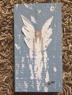 an angel painted on a piece of wood with white paint and brown hair is sitting on the ground