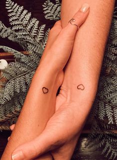 two hands holding each other with small tattoos on their arms and legs, one has an arrow in the middle