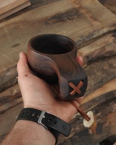 a hand holding a wooden cup with a cross on the side and spoon in it