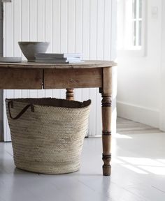 a table with a basket underneath it on the floor next to a bowl and cup